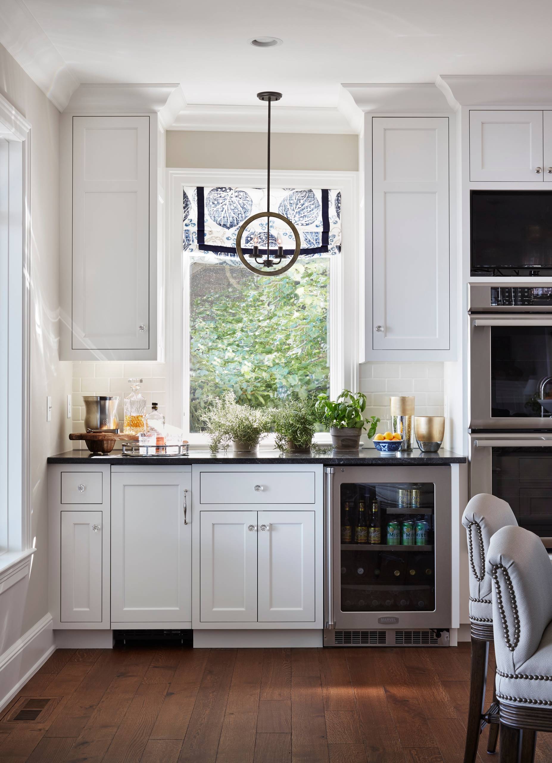 White shaker cabinets, black countertop, subway tile, and wood floors in a refined kitchen beverage station.
