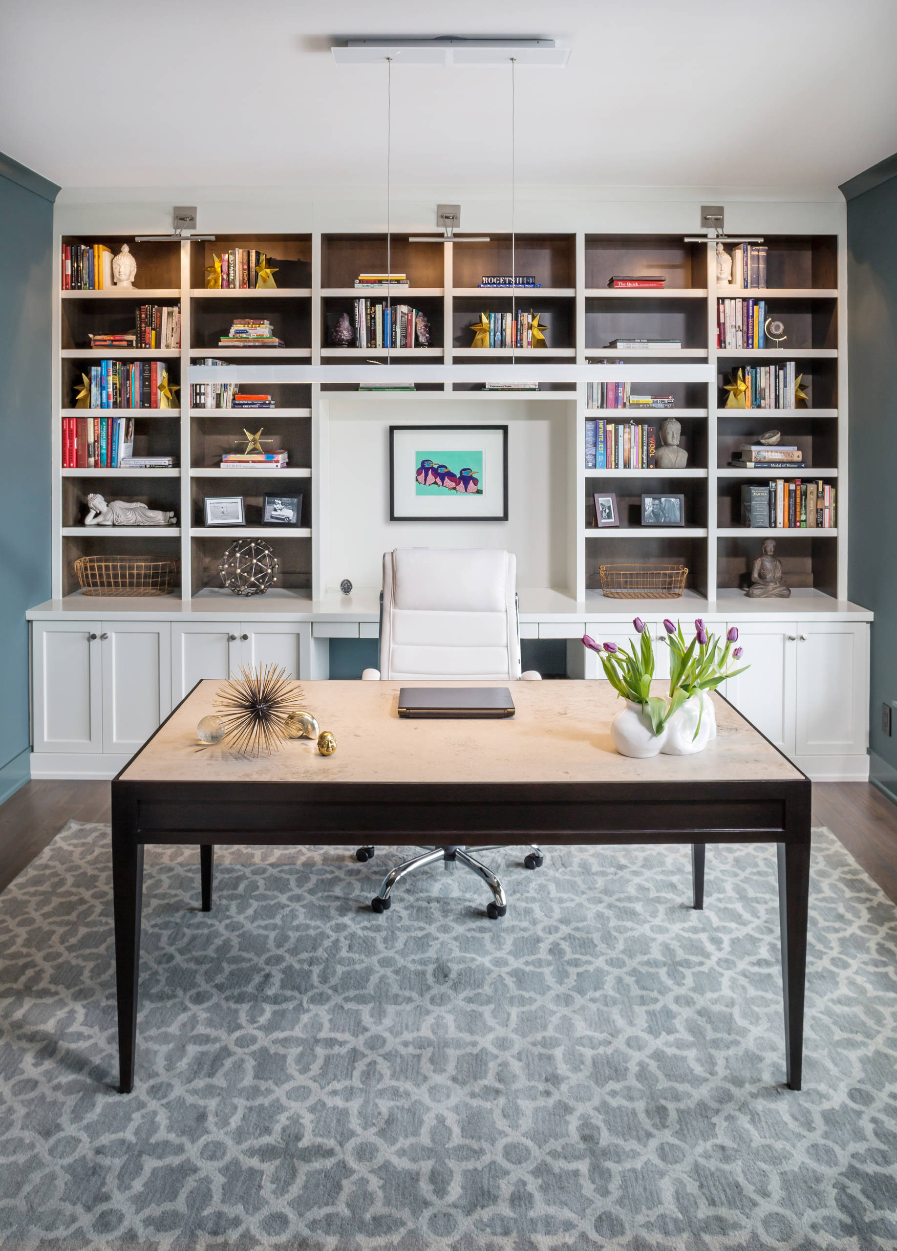 Bright home office with white built-in bookshelves, teal accent walls, dark wood desk, and gray patterned rug.