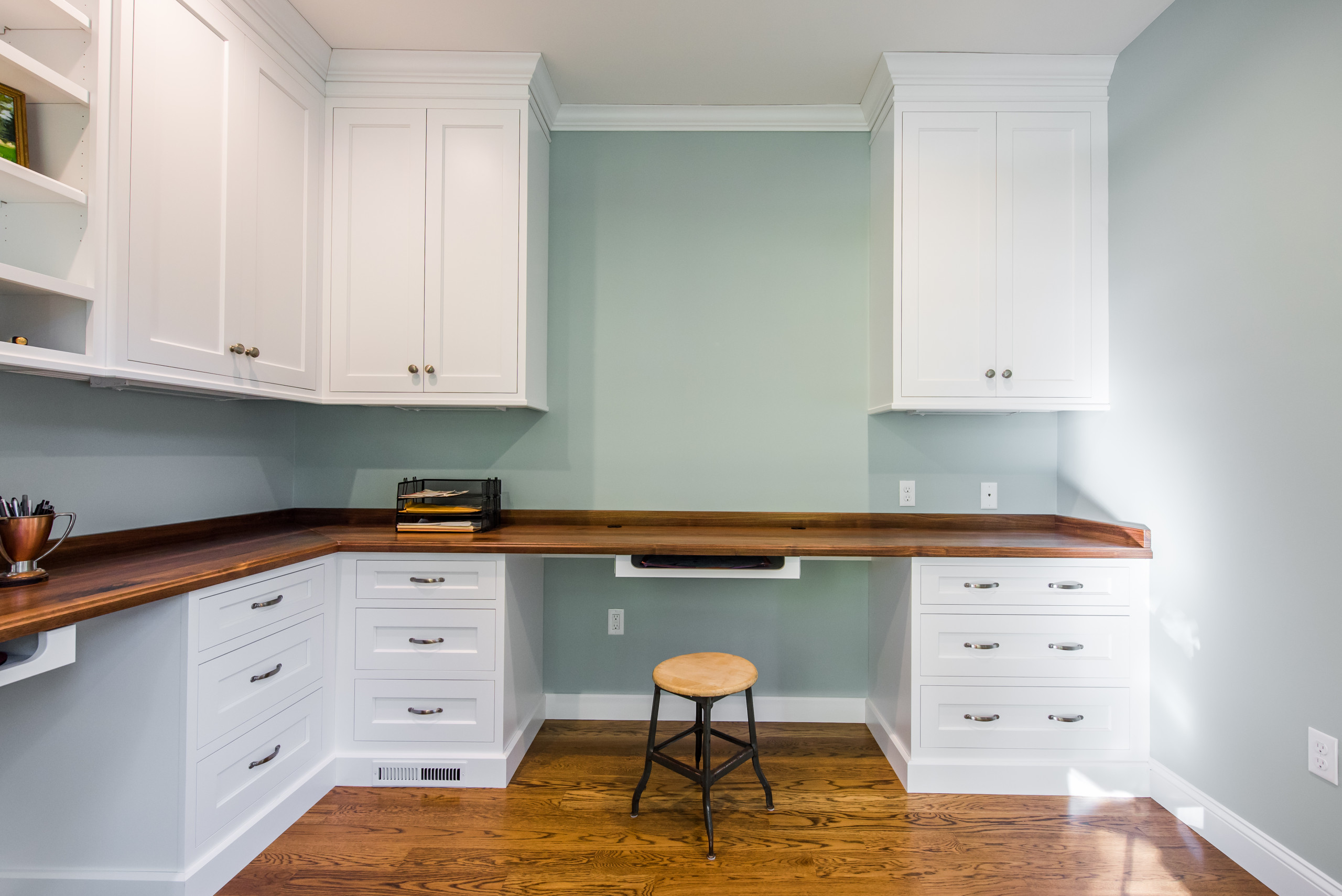 Bright study nook with white shaker cabinets, warm wood countertop, and pale blue-green walls.