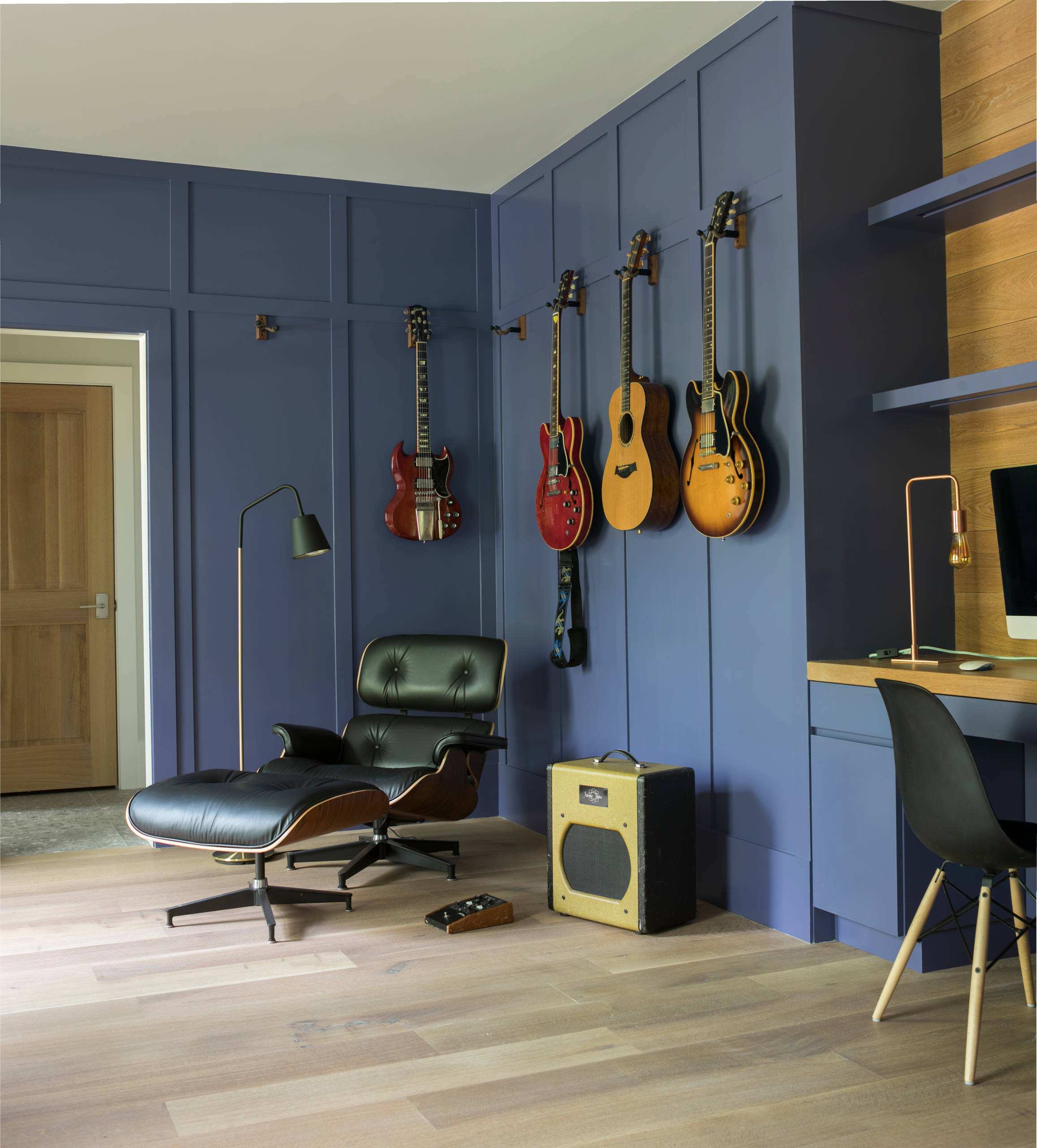 Vibrant indigo paneled walls showcase guitars, complementing a black leather lounge chair and light wood desk.