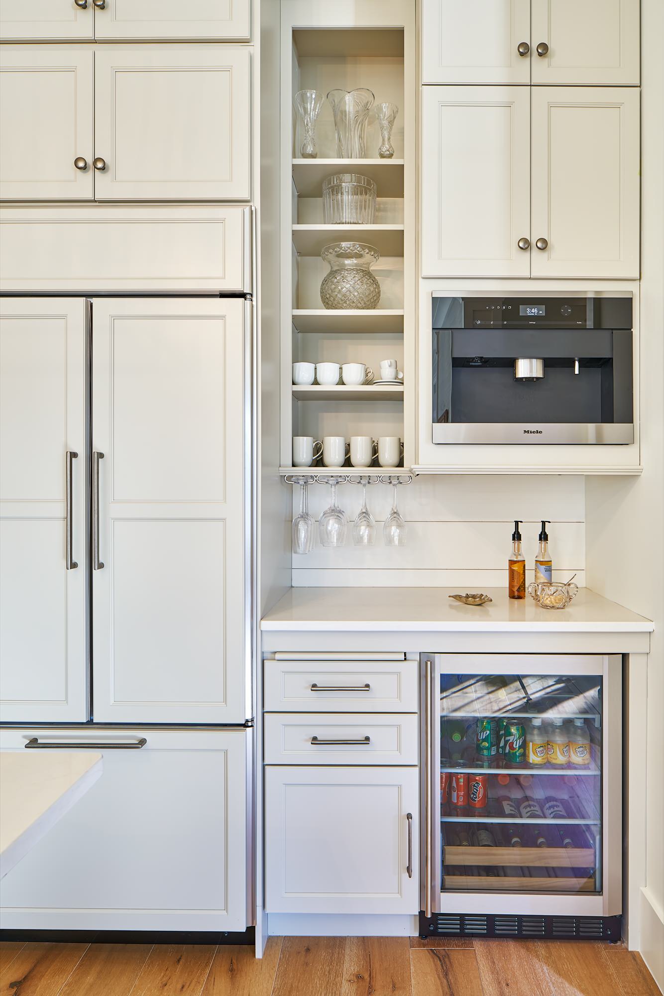 Bright kitchen corner with white cabinets, integrated refrigerator, Miele coffee maker, open shelving, and beverage fridge.