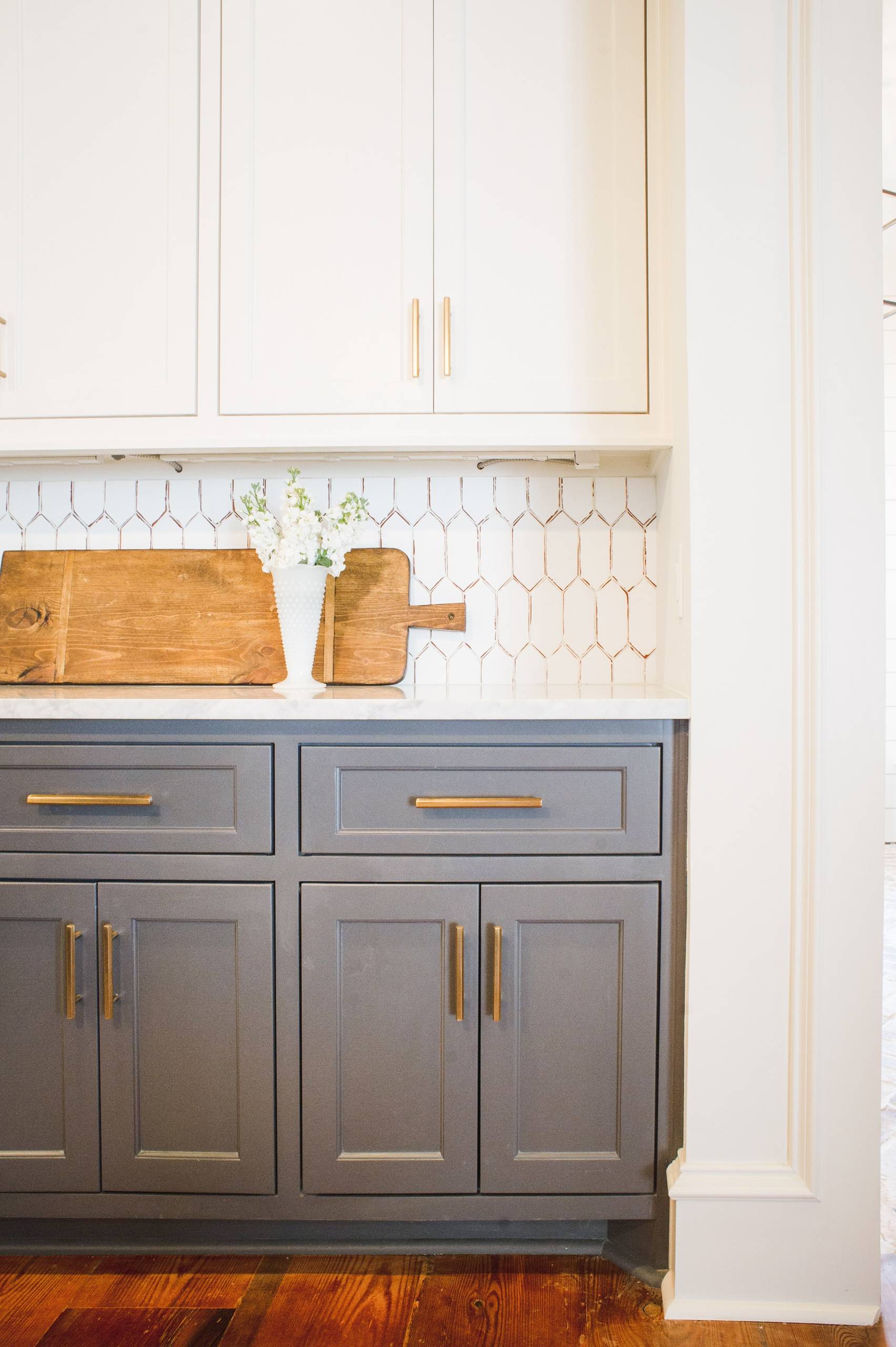 Bright kitchen with white upper cabinets, gray lower cabinets, gold hardware, and a unique hexagonal tile backsplash.