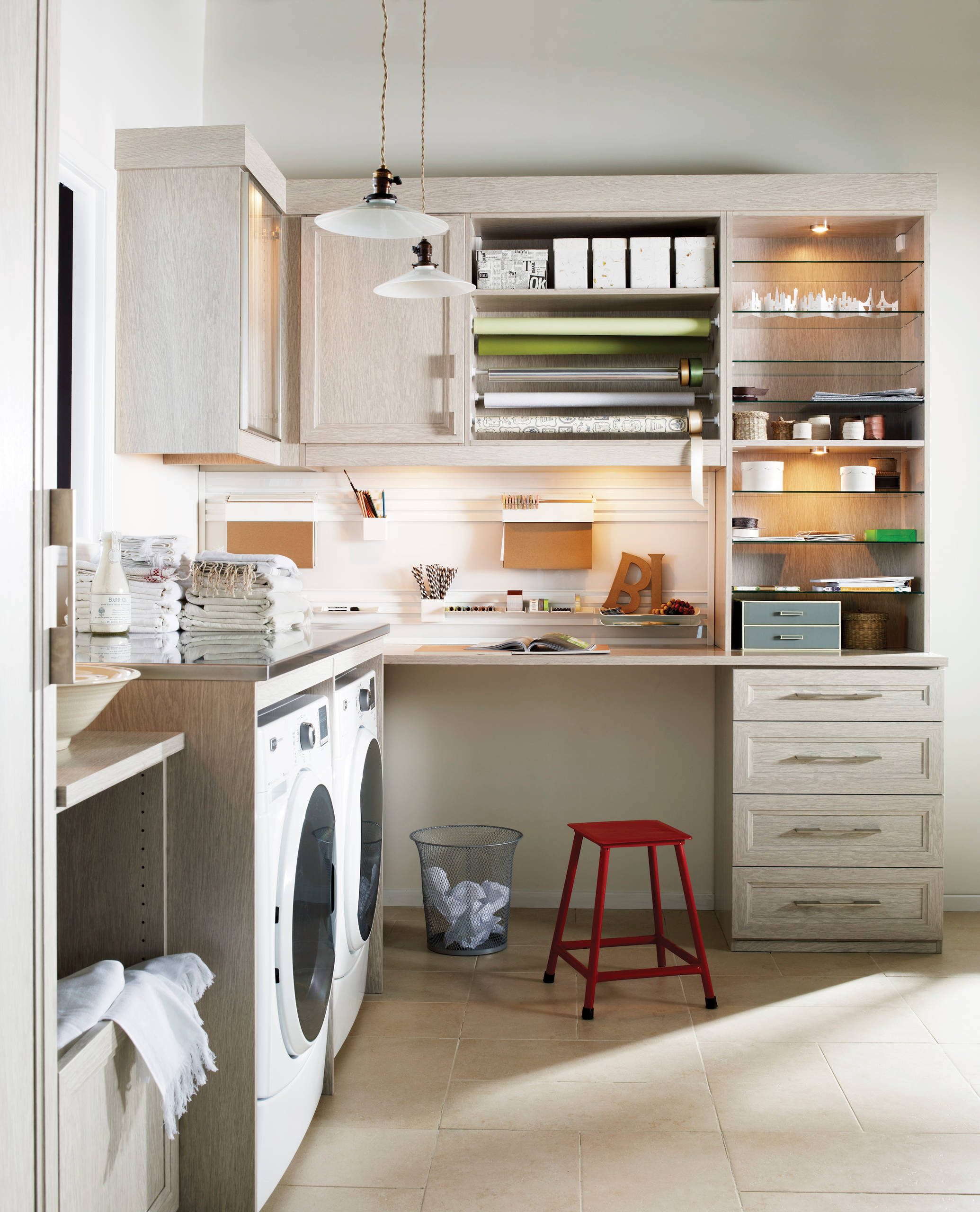Bright, organized laundry room with integrated craft station, light wood cabinetry, and beige tile flooring.