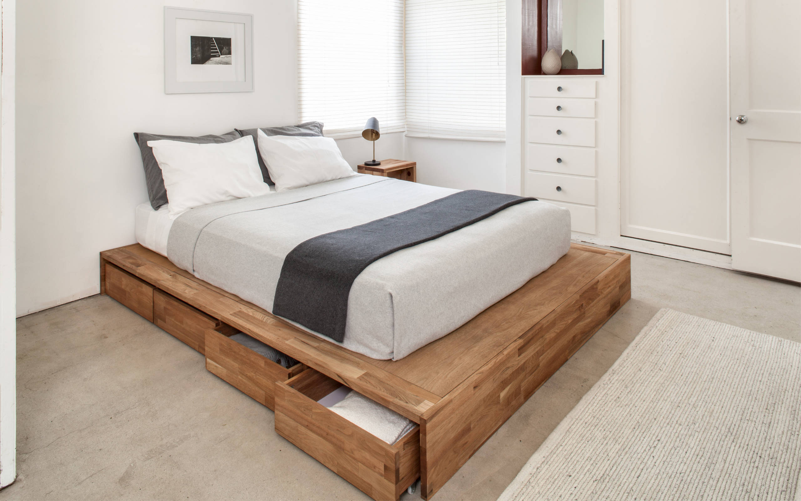 Light-filled bedroom with a natural wood platform bed, integrated storage, and simple white linens.