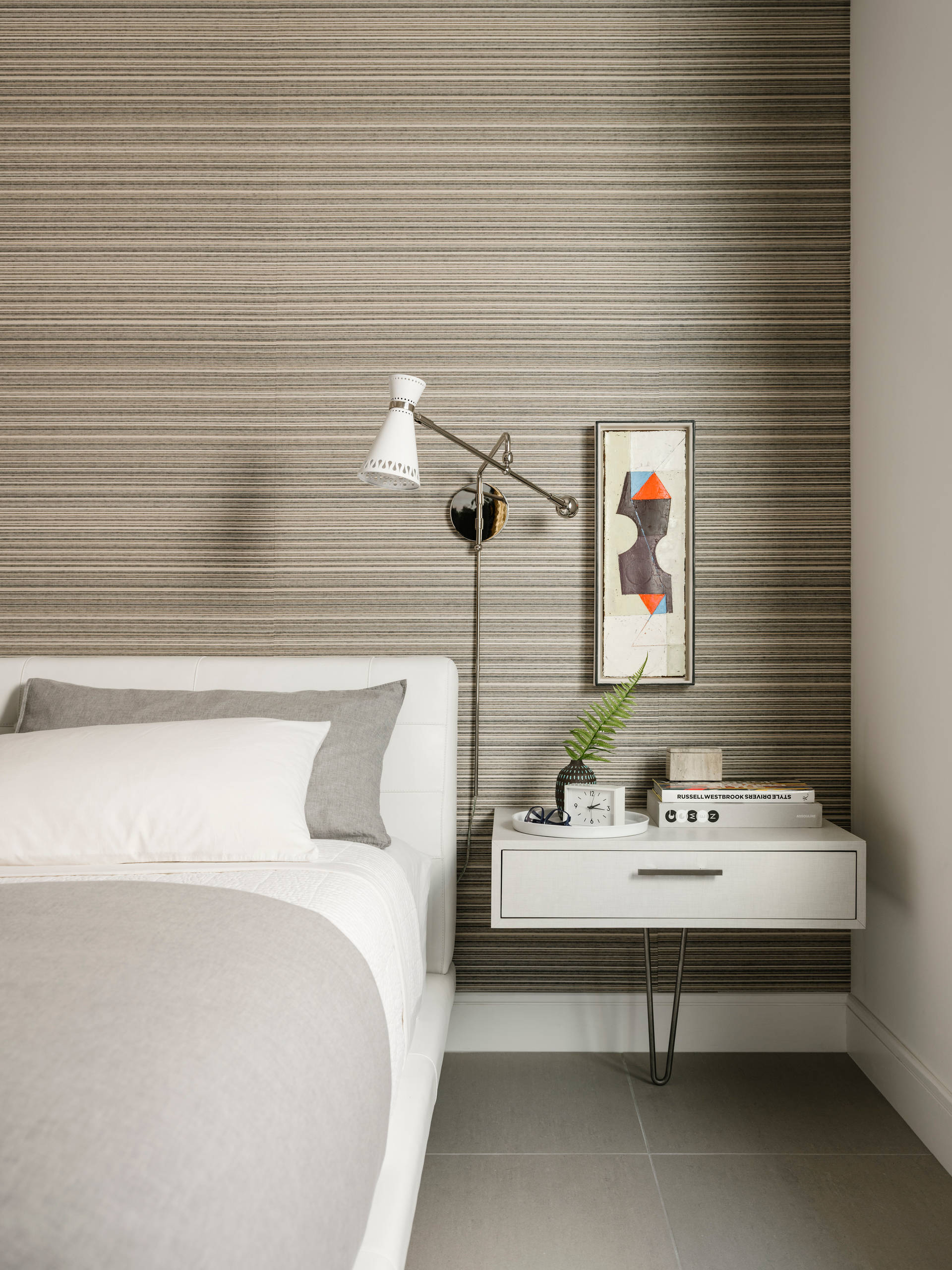 Modern bedroom with horizontal striped wallpaper, white upholstered bed, floating nightstand, and geometric art.