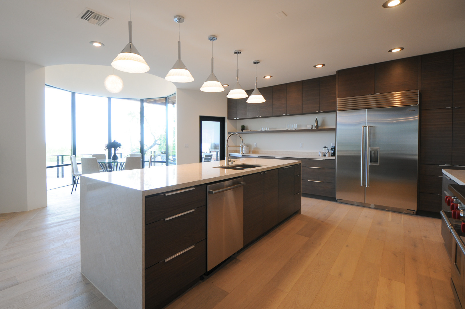 Spacious kitchen with dark wood cabinetry, light wood flooring, a long island, and stainless steel appliances.