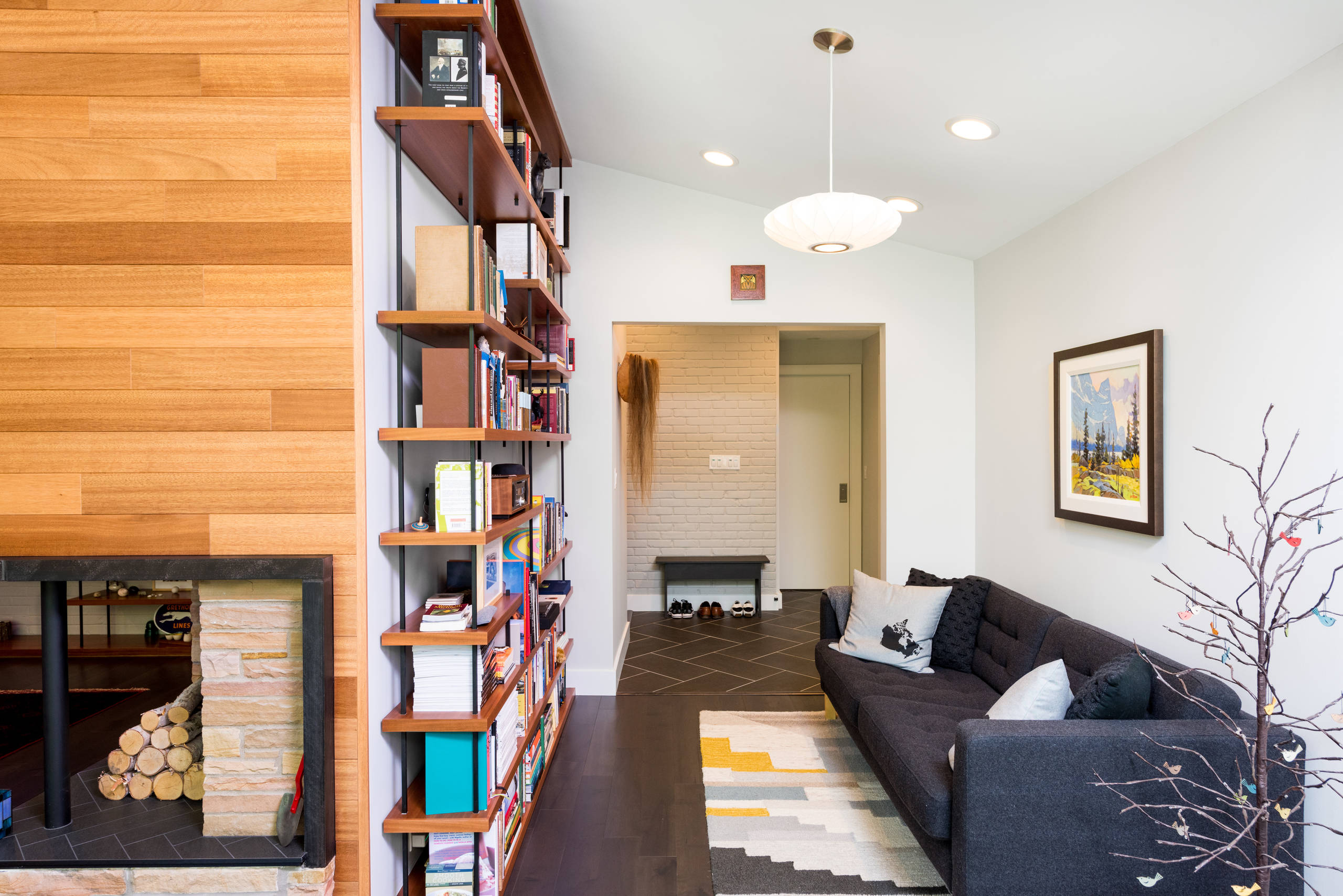 Modern living room with wood paneling, built-in shelves, dark sofa, and a fireplace with stacked logs.