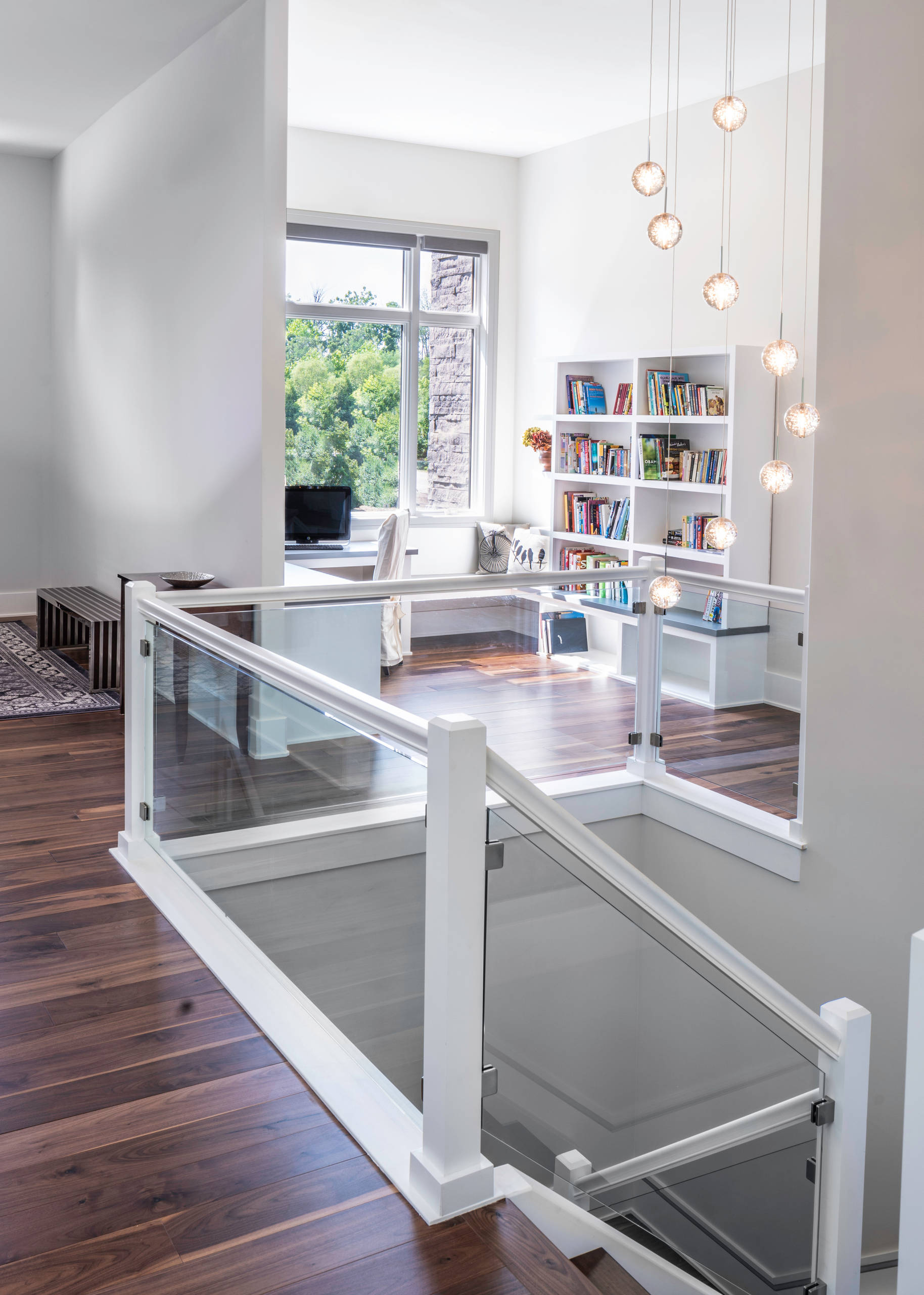 Bright modern loft study with white built-in bookshelves, large window, wood flooring, and sculptural pendant lights.