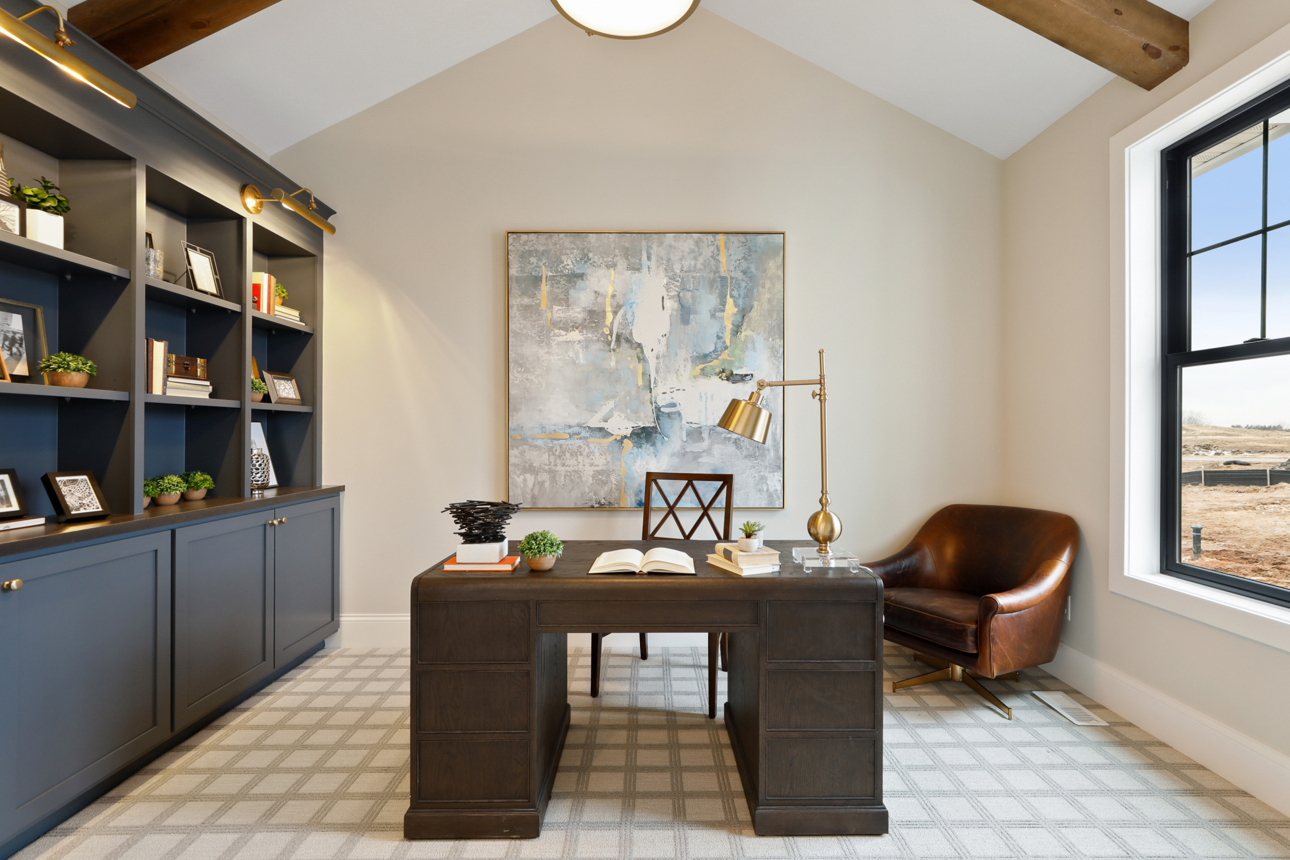Home office with dark wood desk, built-in navy shelving, brown leather chair, patterned carpet, and light walls.
