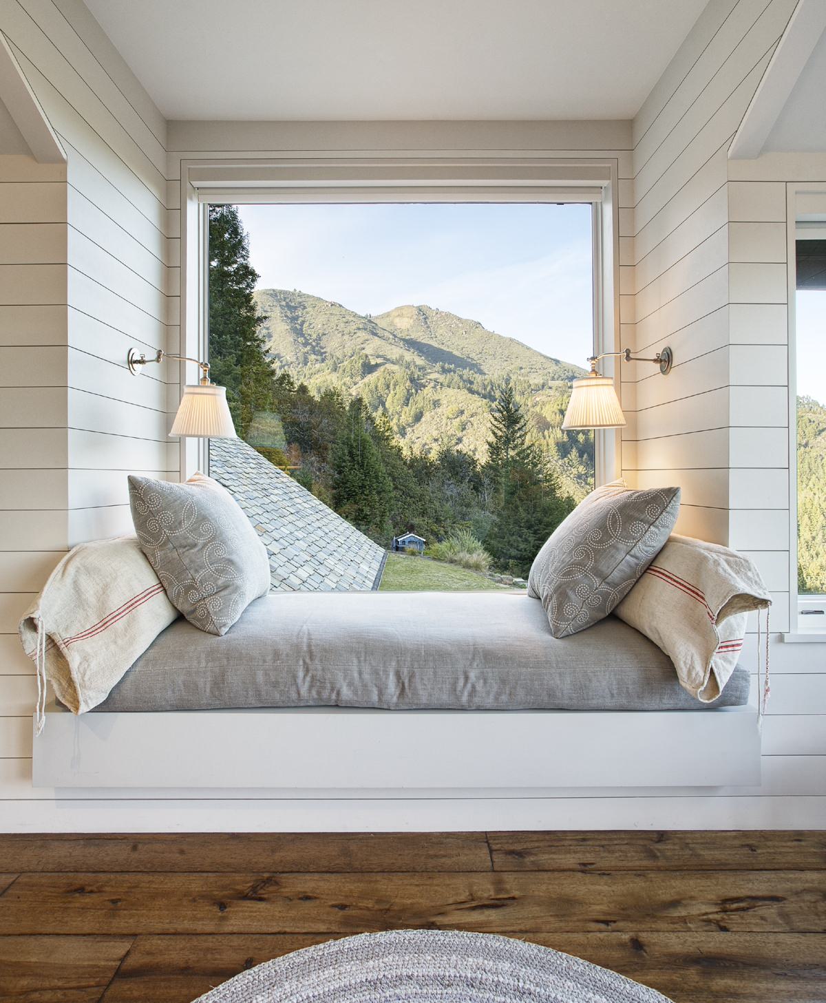 A serene window seat with a large mountain view, shiplap walls, and swing-arm sconces.