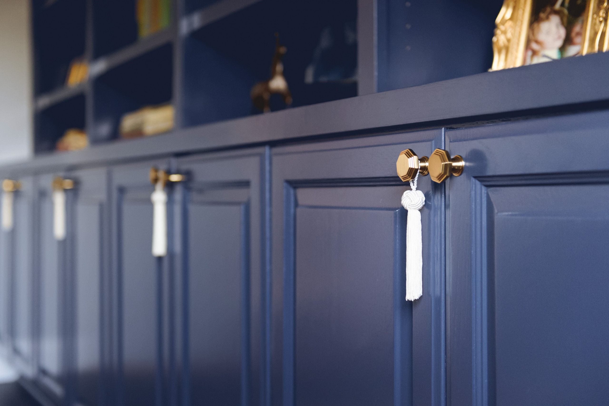 Close-up of navy built-in cabinets with octagonal gold knobs and decorative white tassels, featuring open shelving above.