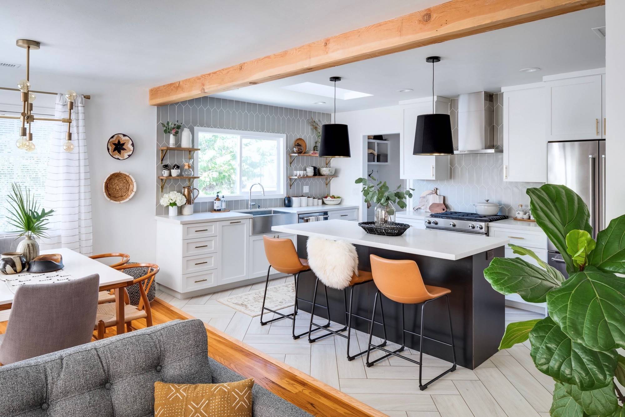 Open concept kitchen with light gray tile backsplash, black island, white cabinets, and wood accents.