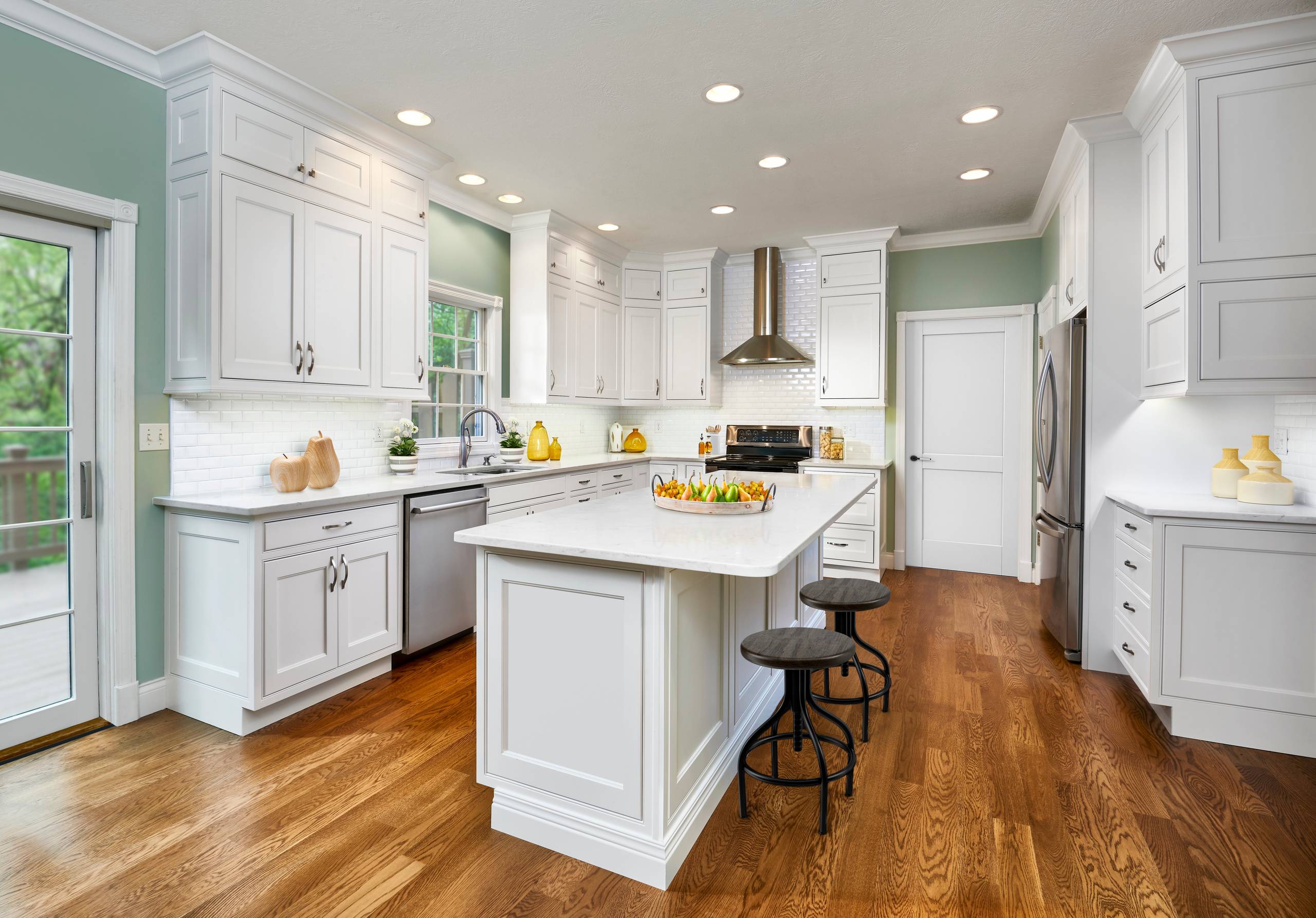 Bright kitchen with white shaker cabinets, pale green walls, white quartz countertops, and a central island.
