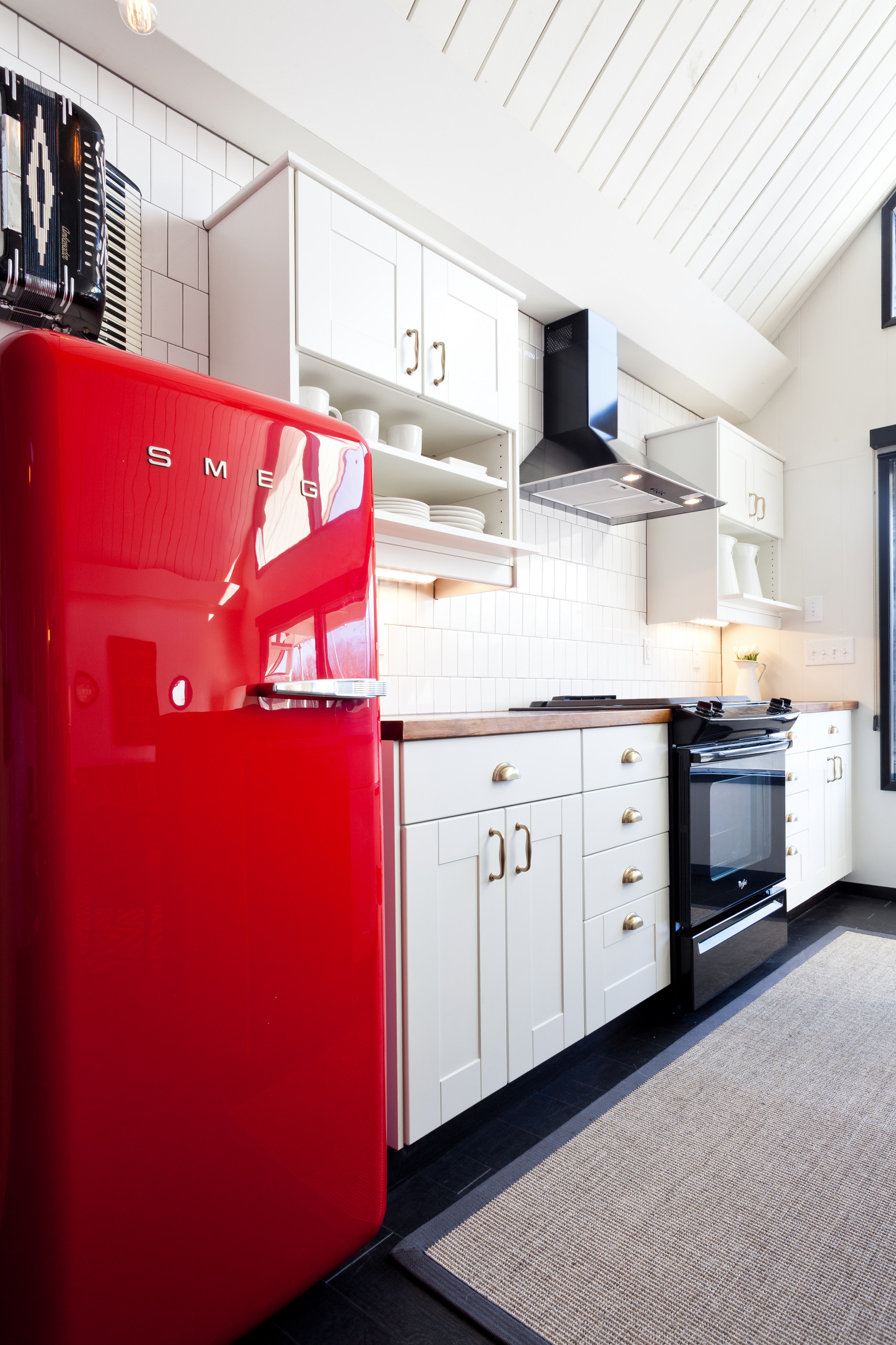 Kitchen with bold red Smeg refrigerator, white shaker cabinets, subway tile backsplash, dark wood floors, and brass hardware.