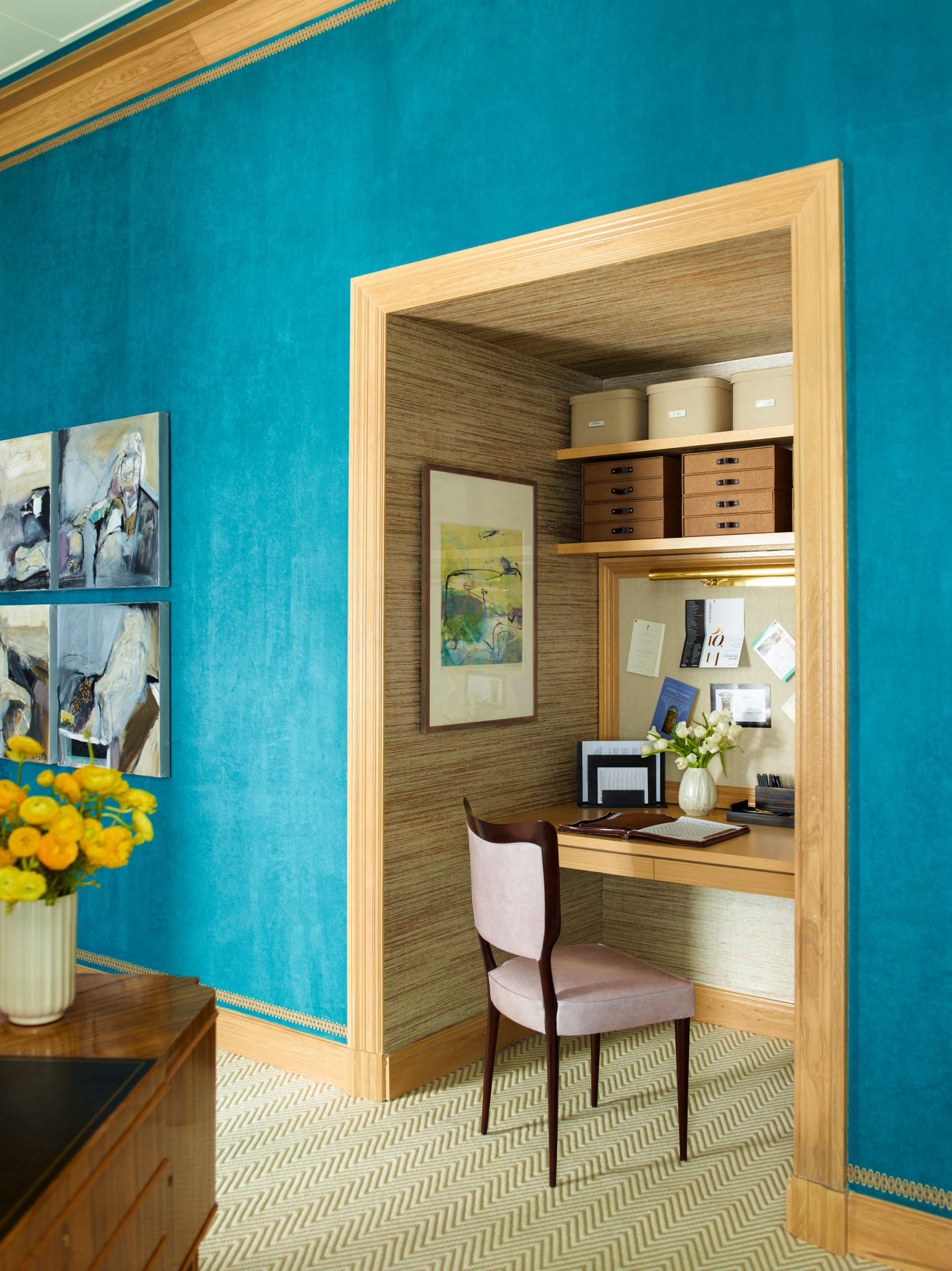 Teal blue walls frame a warm wood alcove office with grasscloth, built-in desk, and storage shelves.