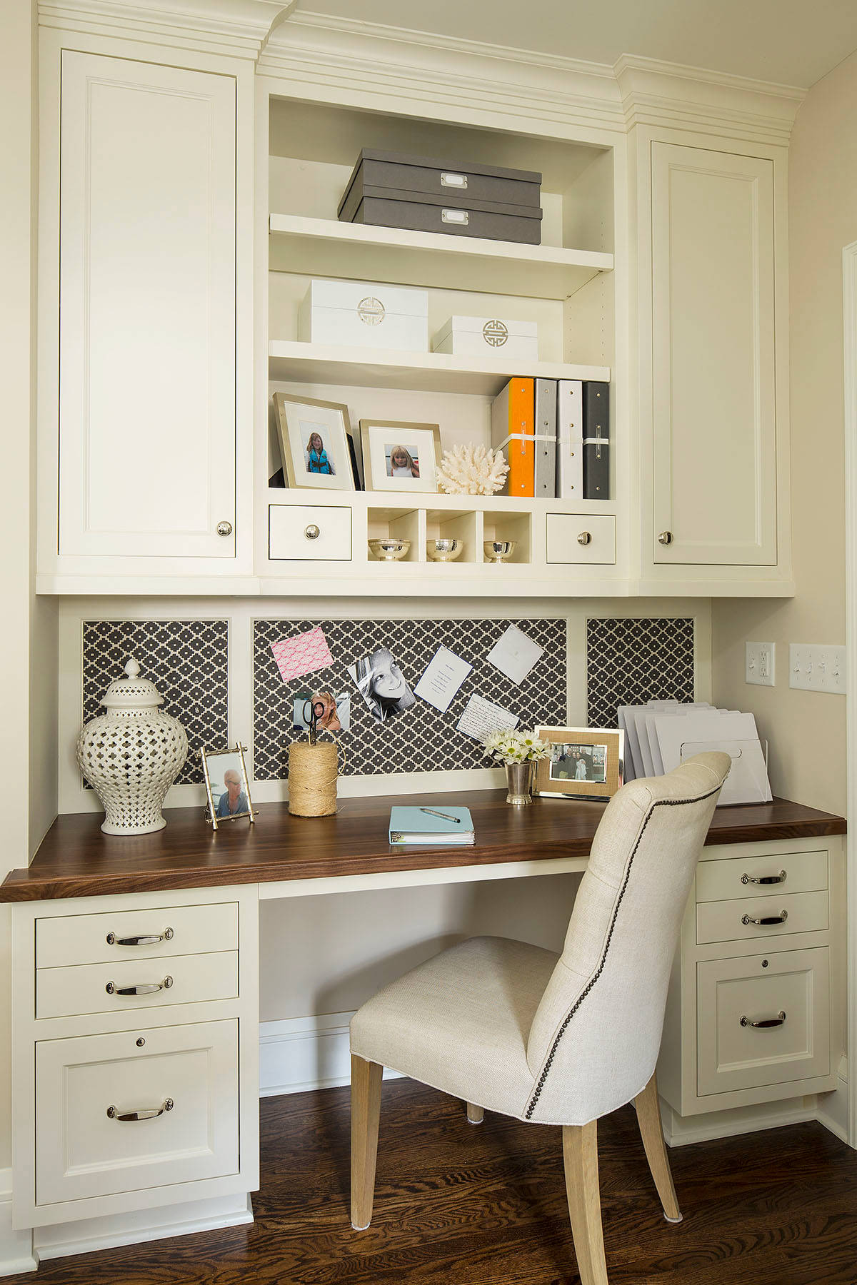 Traditional home office with cream built-in cabinetry, dark walnut desk, linen chair, and patterned backsplash.