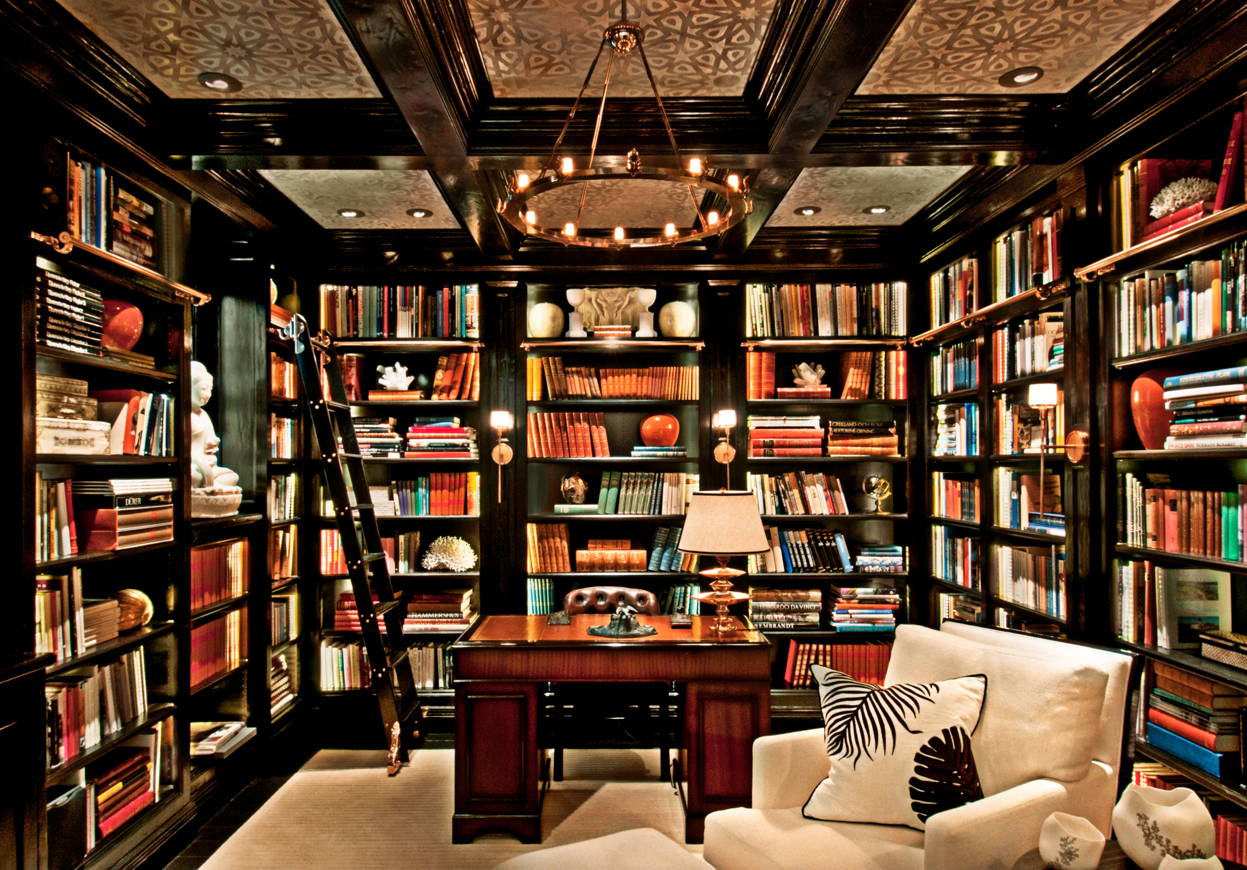 Luxurious traditional library with dark wood built-in bookshelves, central desk, and cream armchair.