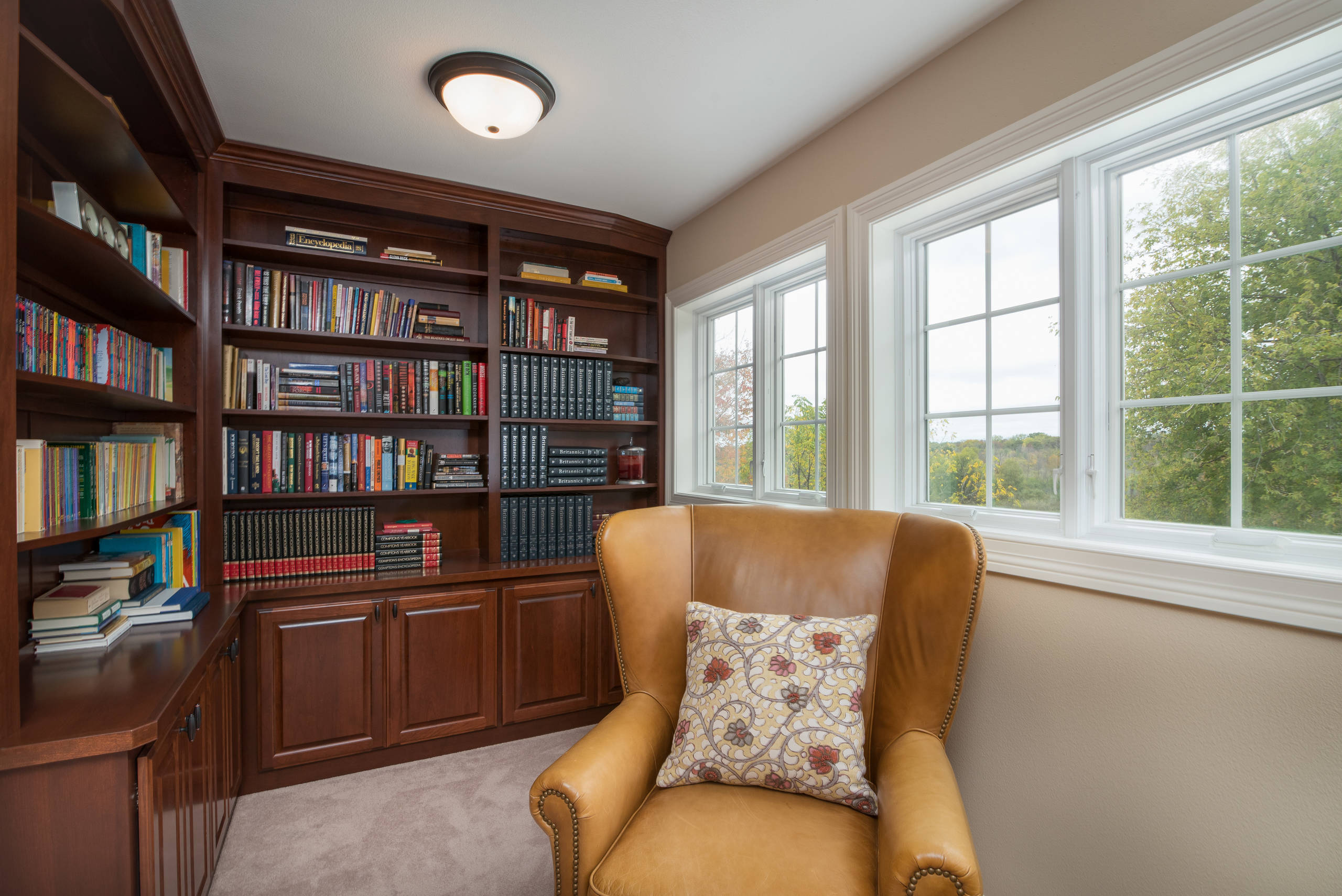 Cozy reading nook with dark wood built-in bookshelves, tan leather armchair, and large windows.