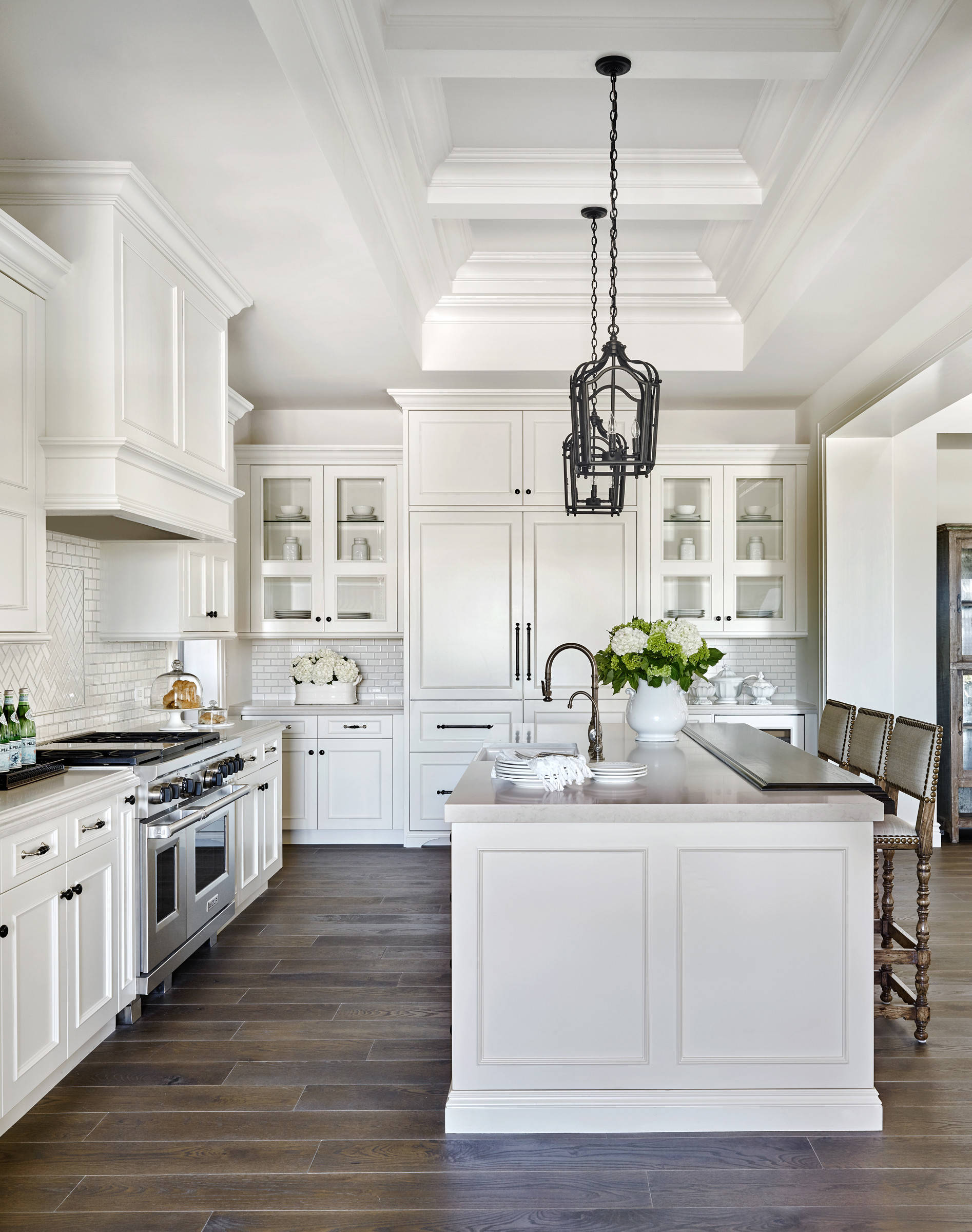 Bright white traditional kitchen with dark wood floors, coffered ceiling, and central island.