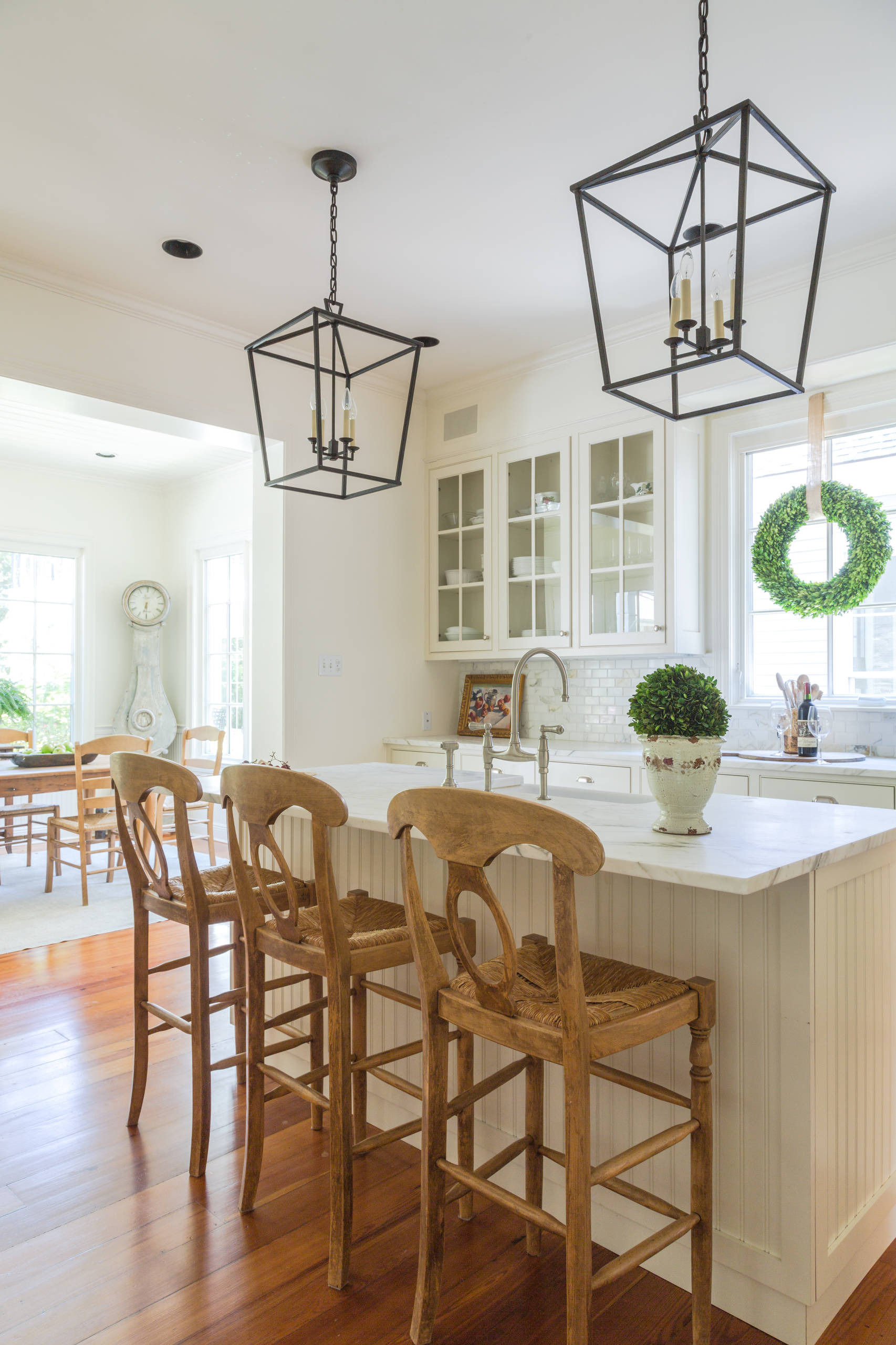 Classic white kitchen with a marble-topped island, wooden barstools, and black lantern pendant lights.