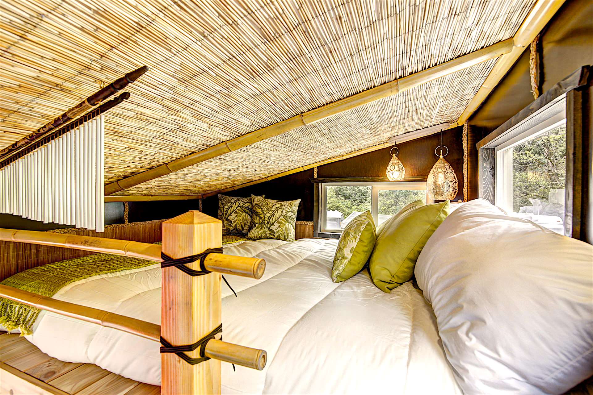 Cozy loft bedroom featuring a bamboo slatted ceiling, white bedding, and green accent pillows.