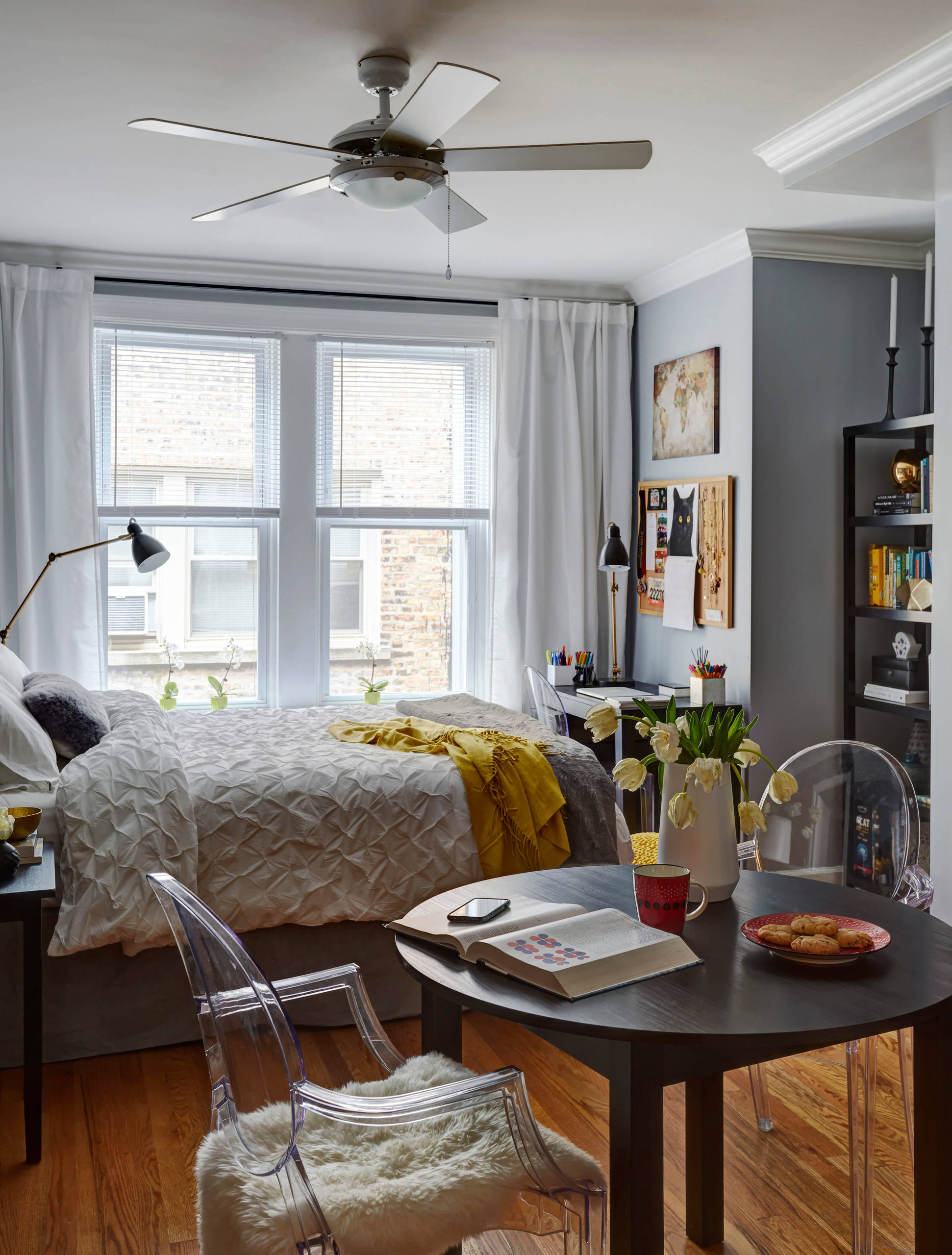 Compact urban bedroom featuring a bed, desk, and dining area, with a muted color palette.