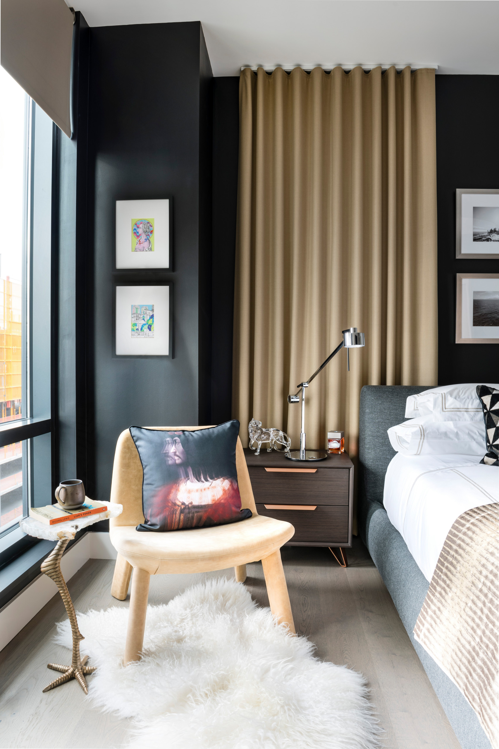 Modern bedroom with black walls, gold curtains, grey bed, light wood floors, and mixed art.