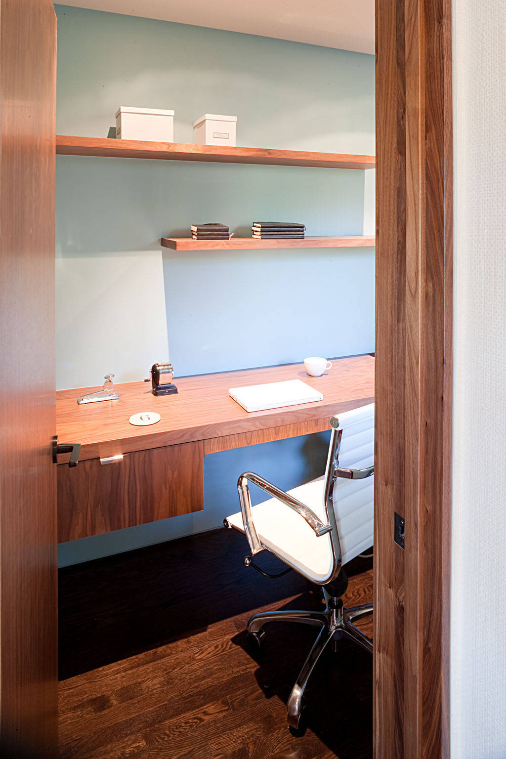Warm walnut wood desk and floating shelves set against a light blue wall in a compact home office.