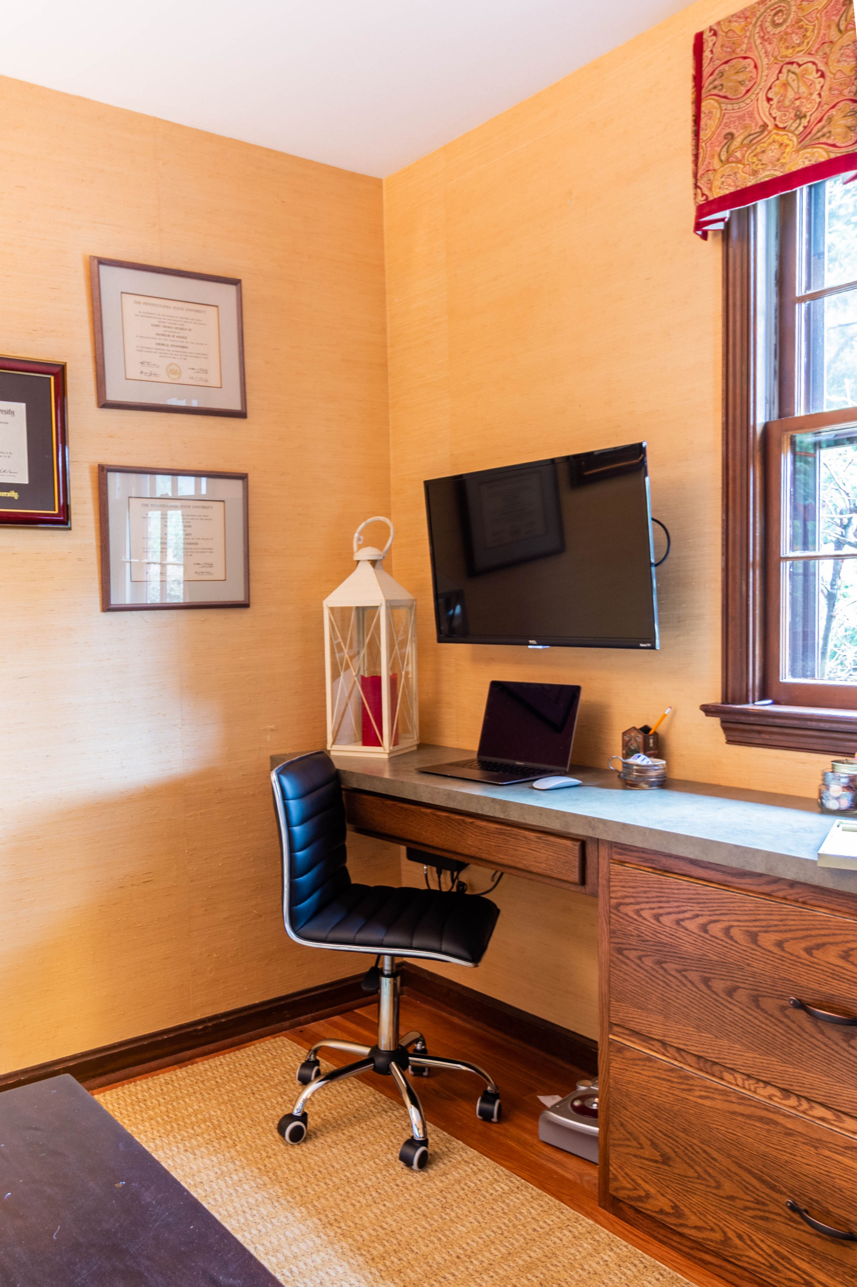 A cozy home office features textured ochre walls, a natural wood desk with built-in storage, and a black ergonomic chair.