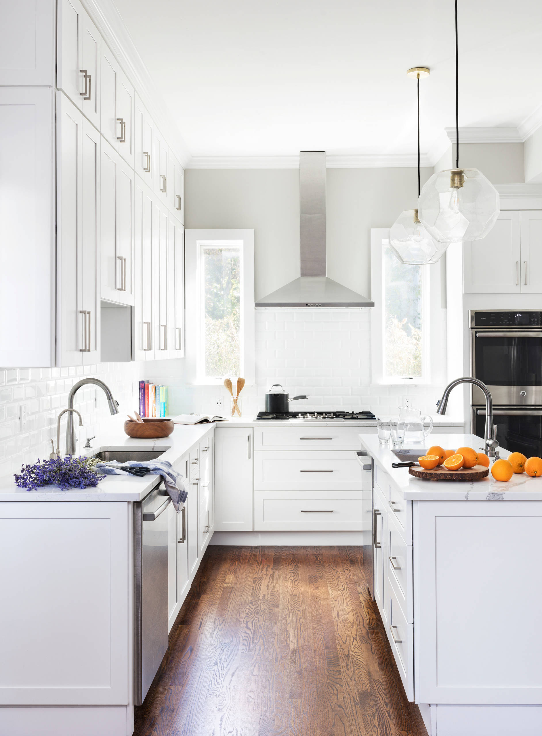 Bright white kitchen with shaker cabinets, subway tile, dark wood floor, and clear geometric pendant lights.
