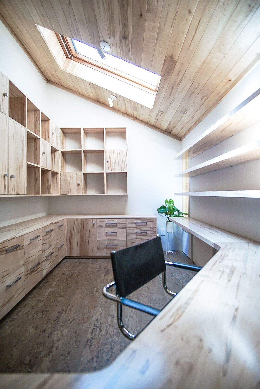 Bright home office with light wood cabinetry, desk, and shelves, slanted wood ceiling with a skylight.